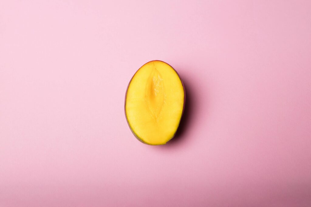 Half sliced mango placed on a soft pink background in a minimal flat lay style.