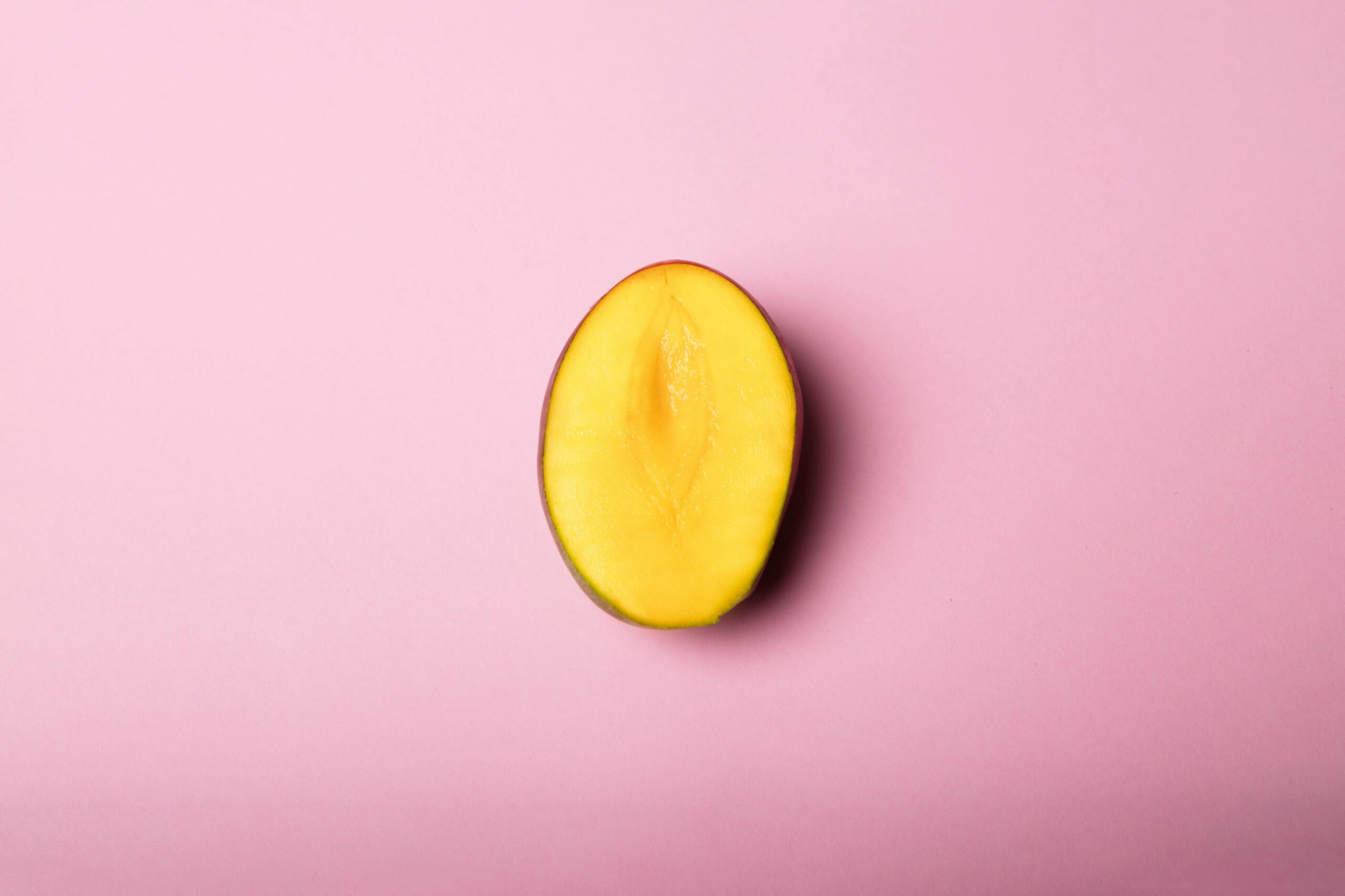 Half sliced mango placed on a soft pink background in a minimal flat lay style.