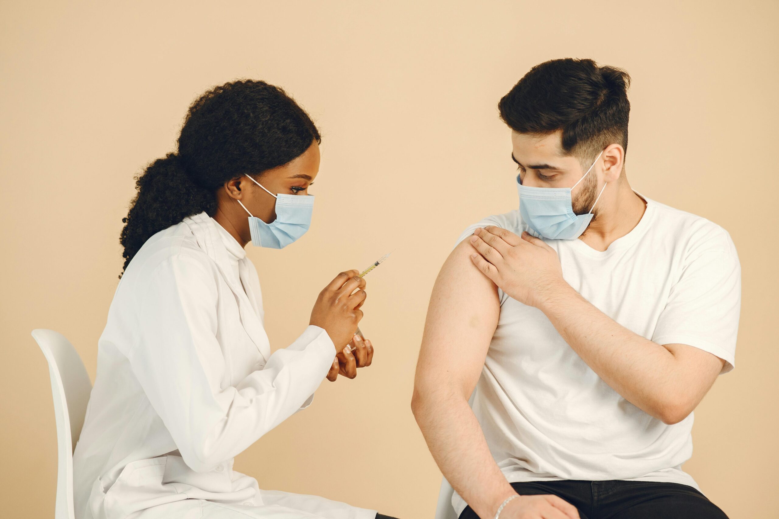 Doctor giving a vaccination to a patient wearing face masks in a medical setting.